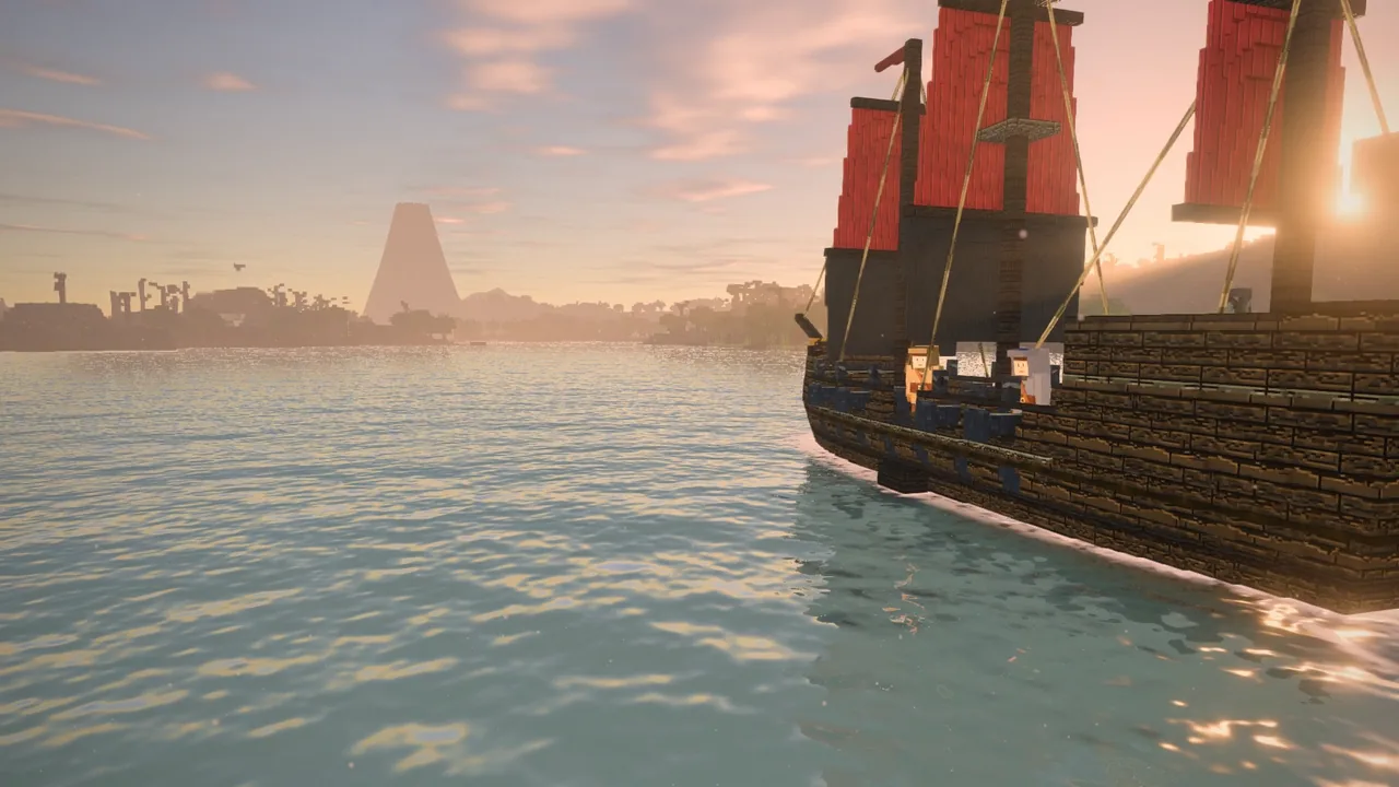 A galleon's red sails lit by the sun, seen from the water beside her